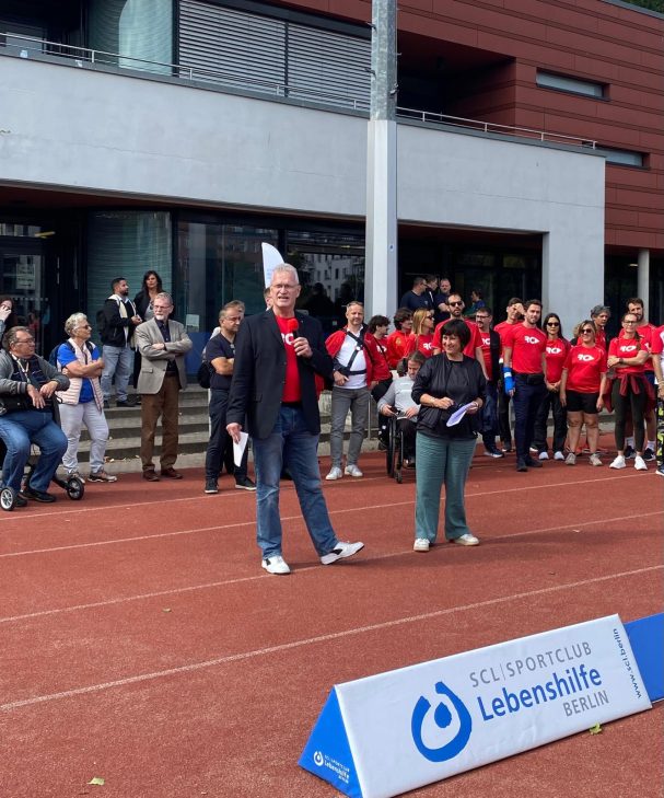 Stefan Schenck und die sport-Staatssekretärin stehen auf einer Tartanbahn mit Mikrofon in der Hand.