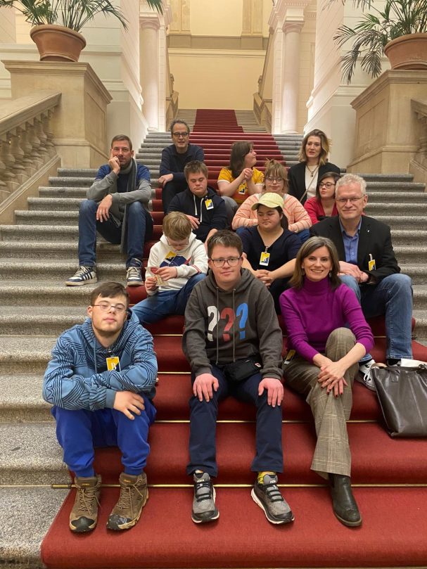eine Gruppe von 12 Menschen sitzt auf dem roten Teppich auf der Treppe im AGH.